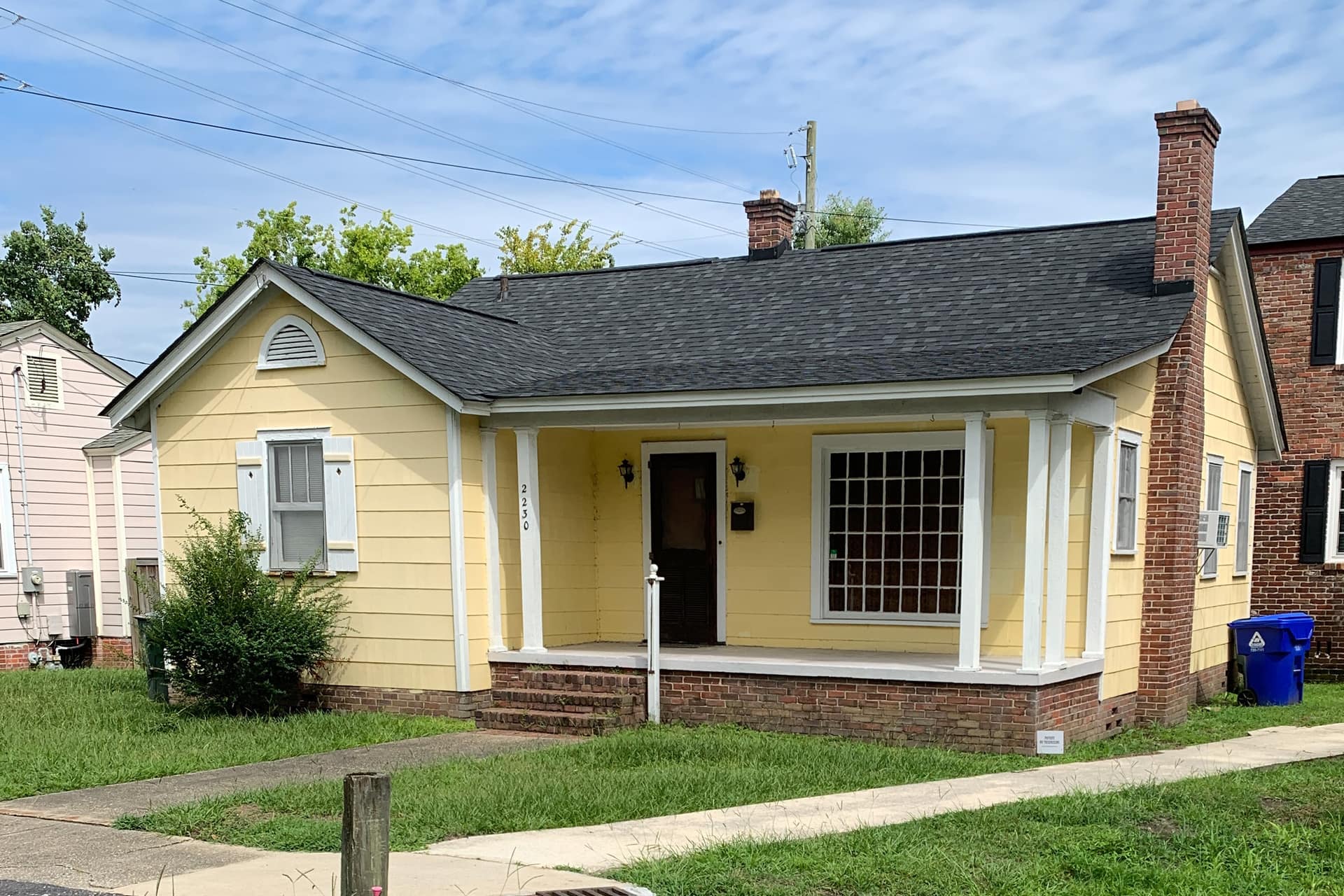 Single-story cottage with a shingle roof, white trim and a covered front porch on a green lawn